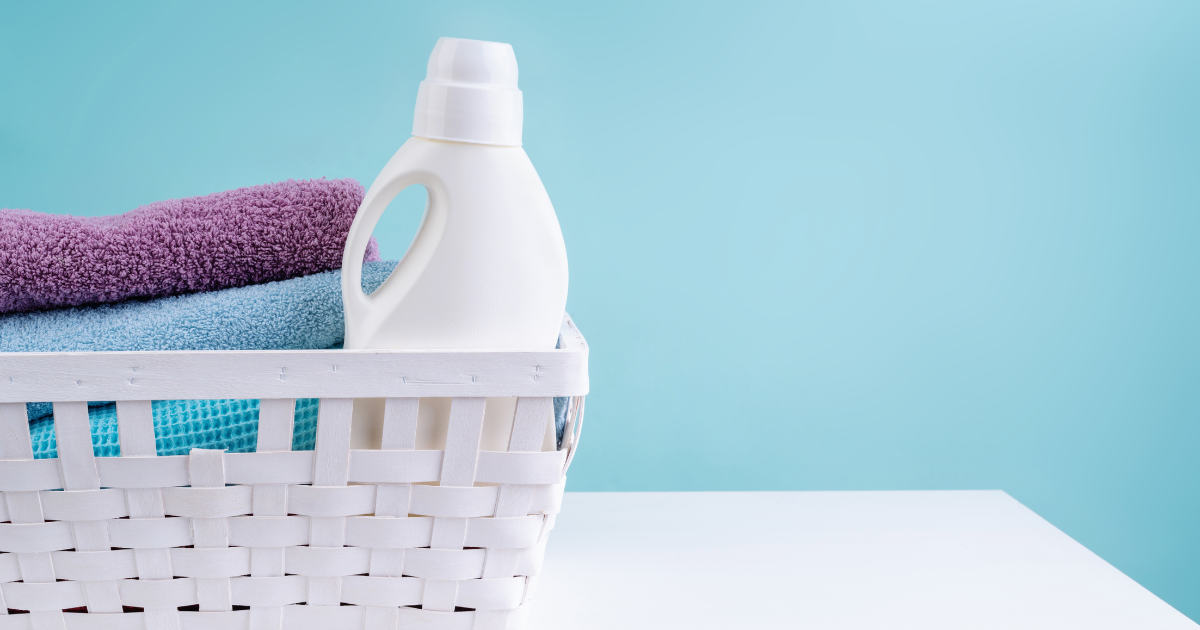 Laundry Service in Charlotte NC - The WashRoom Laundry Service Liquid laundry detergent bottle in a white basket with folded towels, showing the liquid side of the powder vs liquid detergent comparison