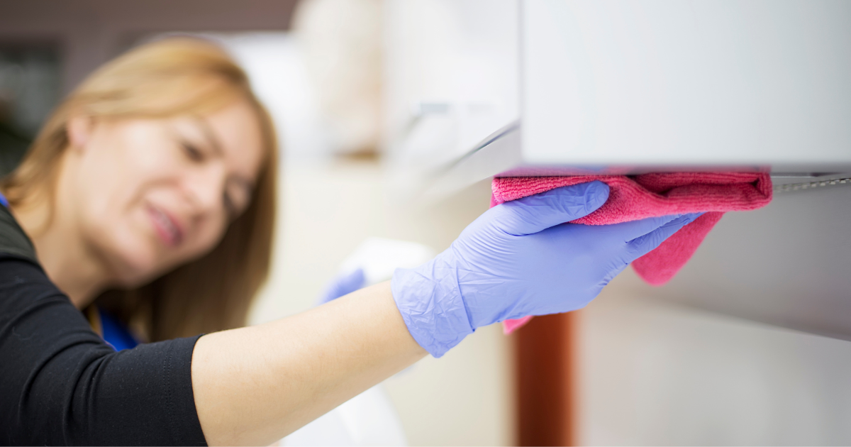 professional laundry service - The WashRoom Laundry Service A cleaning company employee wiping a surface with a pink microfiber cloth, showcasing the high standard of cleanliness achieved when using properly laundered materials from a professional laundry service.