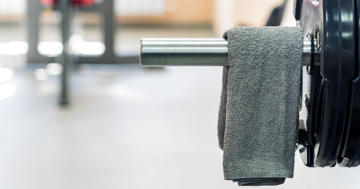A clean, grey gym towel draped over a weightlifting barbell in a fitness center, highlighting the importance of using a professional gym towel laundry service to maintain facility hygiene.