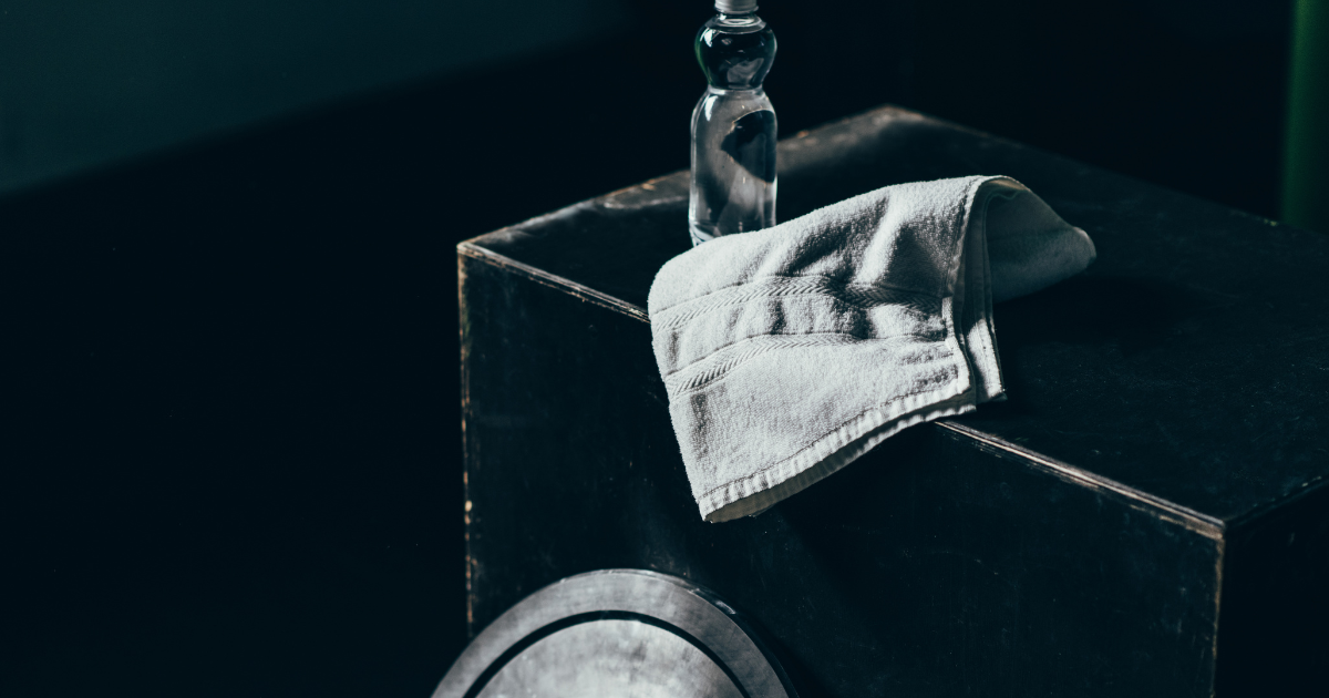 gym towels - The WashRoom Laundry Service A fresh, white gym towel folded neatly on a black workout box next to a water bottle, showcasing the high-quality gym towels provided by WashRoom Laundry’s specialized gym towel service.
