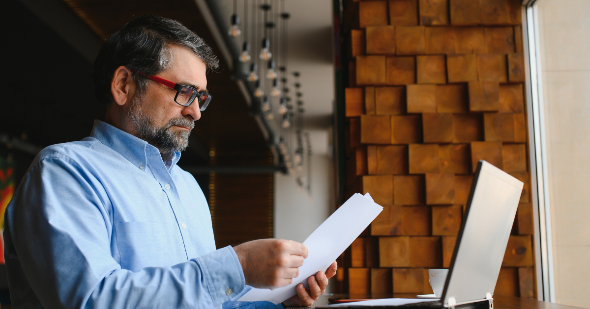 July Blog 1 Pic 1 A business owner, looking focused while reviewing documents at a laptop, symbolizing how outsourcing commercial laundry services frees up valuable time and resources for core business operations.