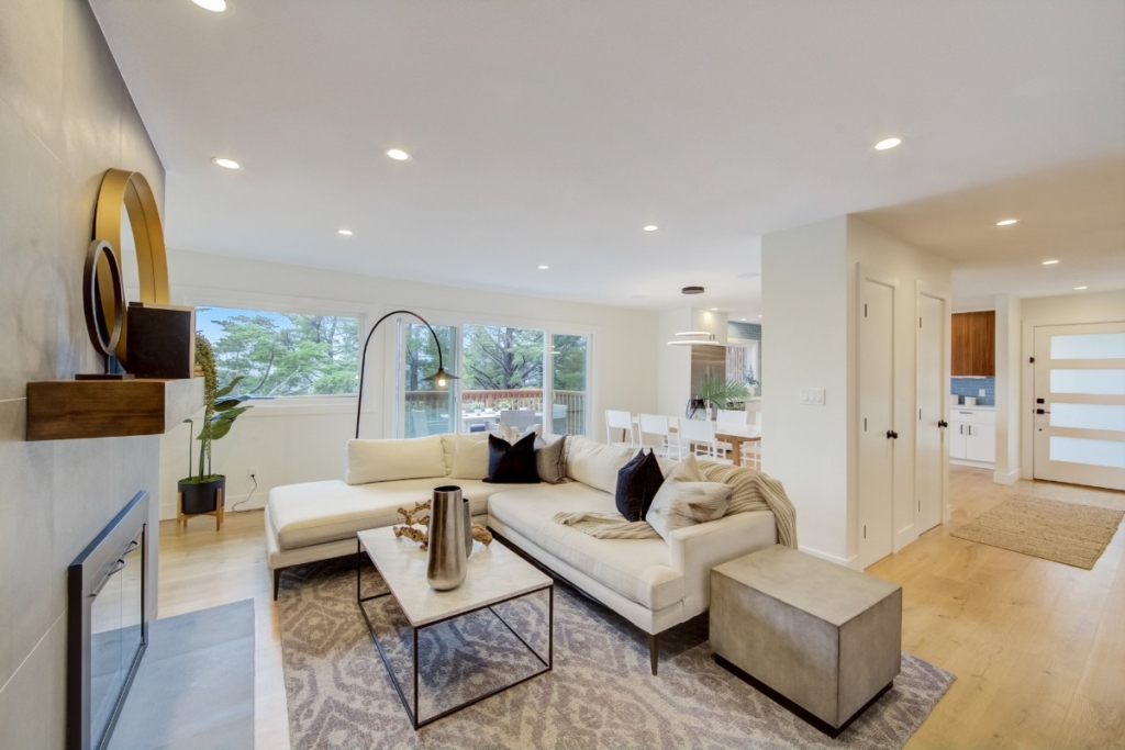 how to clean your house - The WashRoom Laundry Service Bright, modern, and spotless living room with light wood floors and sectional sofa, showing the successful result of house cleaning before selling to appeal to buyers.