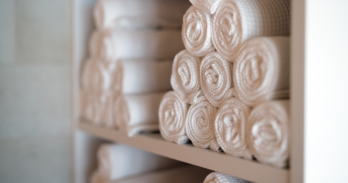 laundry solutions for businesses during flu season - The WashRoom Laundry Service Rolled white commercial linens stacked against a rustic backdrop, illustrating comprehensive laundry solutions for businesses during flu season and the need for rigorous commercial laundry flu disinfection.