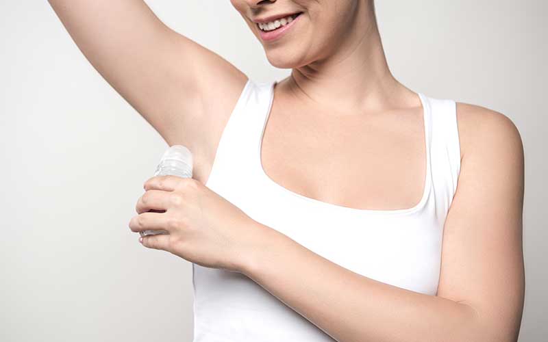 how to eliminate armpit stains - The WashRoom Laundry Service Woman applying underarm antiperspirant while wearing a white shirt to prevent sweat and underarm stains.