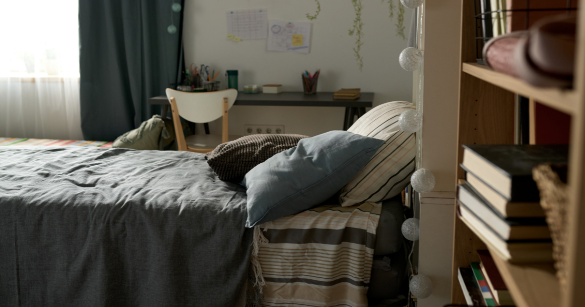 college laundry tips - The WashRoom Laundry Service A small college dorm room with a bed, desk, and bookshelf, showing the limited space students have for laundry essentials.