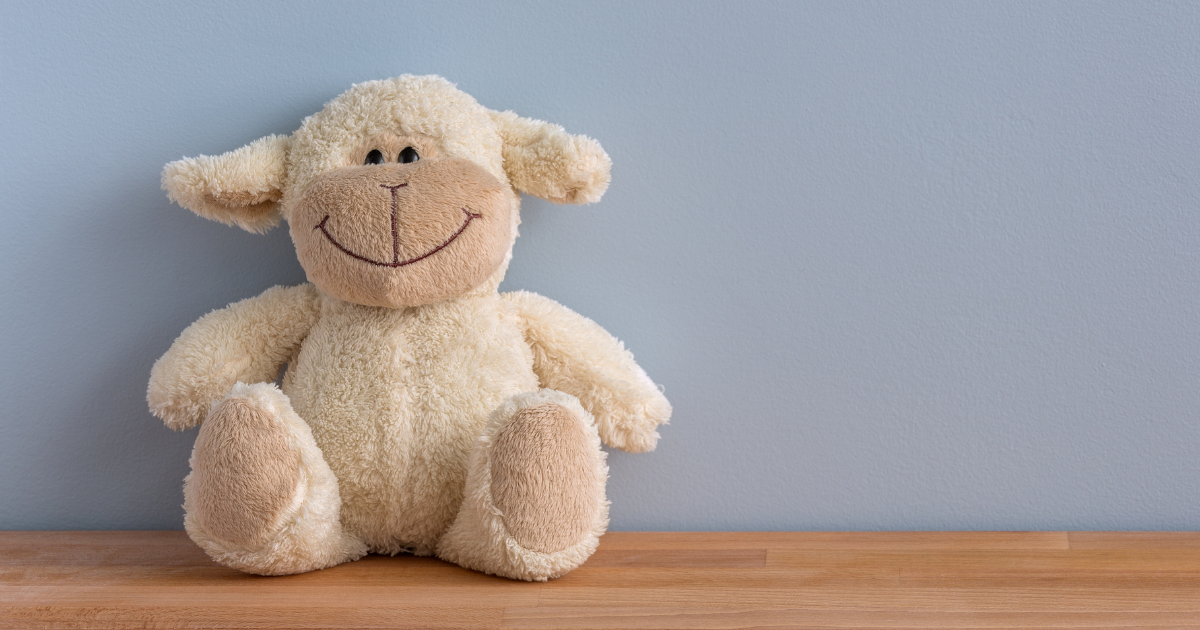 Laundry Service in Charlotte NC - The WashRoom Laundry Service Cream plush lamb sitting on a wooden shelf against a blue wall, a shared daycare toy due for stuffed animal cleaning