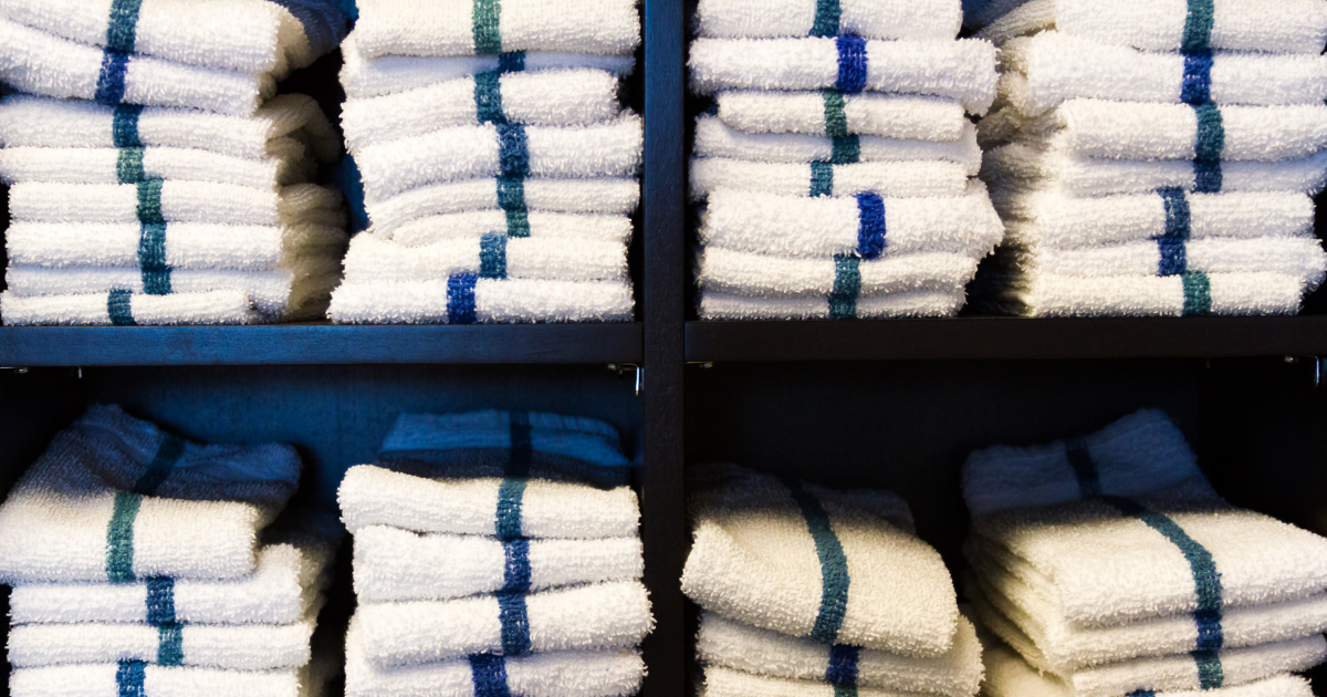 commercial laundry - The WashRoom Laundry Service Neatly folded stacks of white towels with blue and green stripes on a shelf, showcasing professional commercial laundry results for gyms and spas.