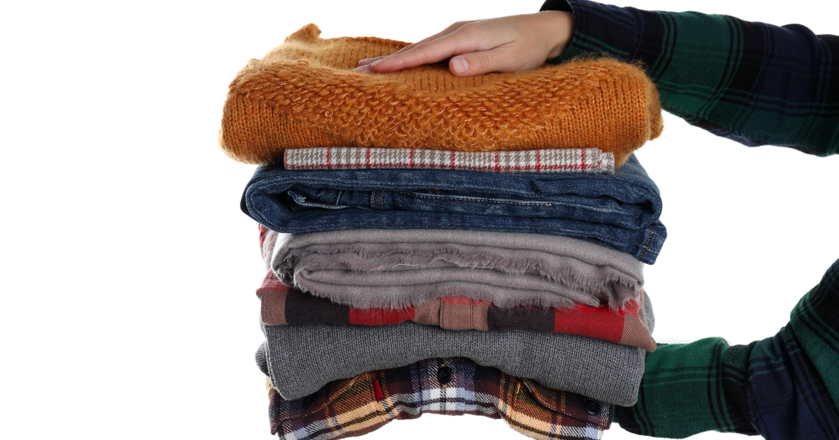Person holding a stack of cleaned clothes after professional textile restoration services
