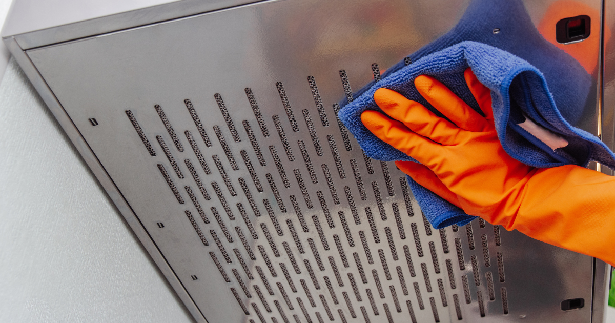 Gloved hand wiping a stainless steel vent hood with a blue microfiber towel during vent hood cleaning