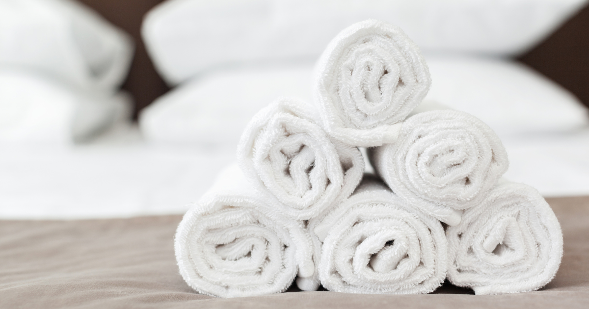 Laundry Service in Charlotte NC - The WashRoom Laundry Service Rolled white towels stacked on a hotel bed after professional hotel linen cleaning