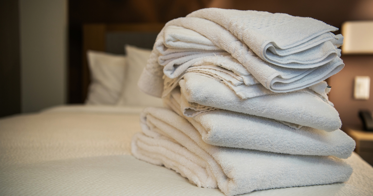 Stack of folded white hotel towels on a guest bed, kept fresh by a commercial laundry service for hotels