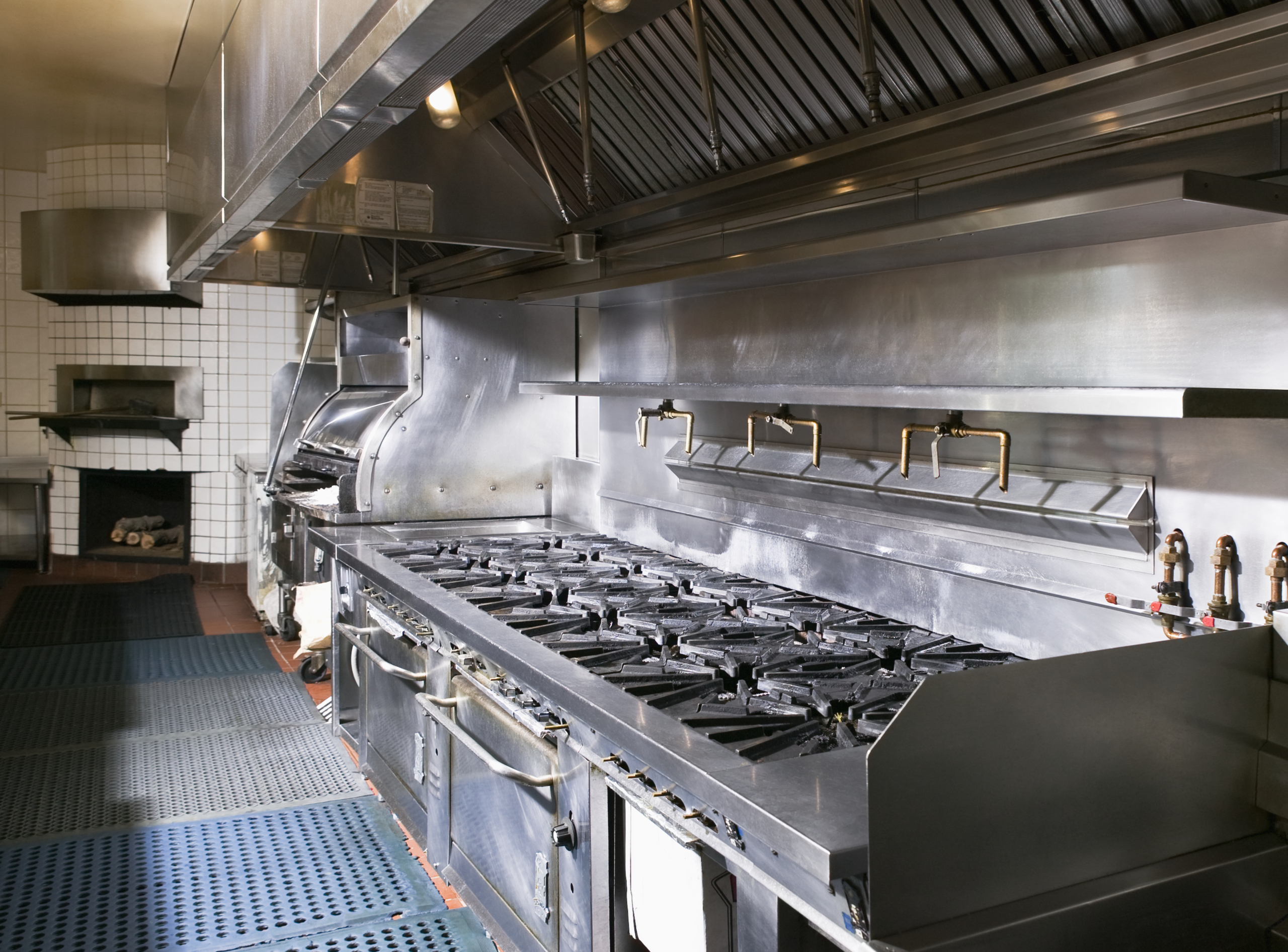 Commercial kitchen floor with anti-fatigue mats and flow-through mats in front of stainless steel cooking equipment